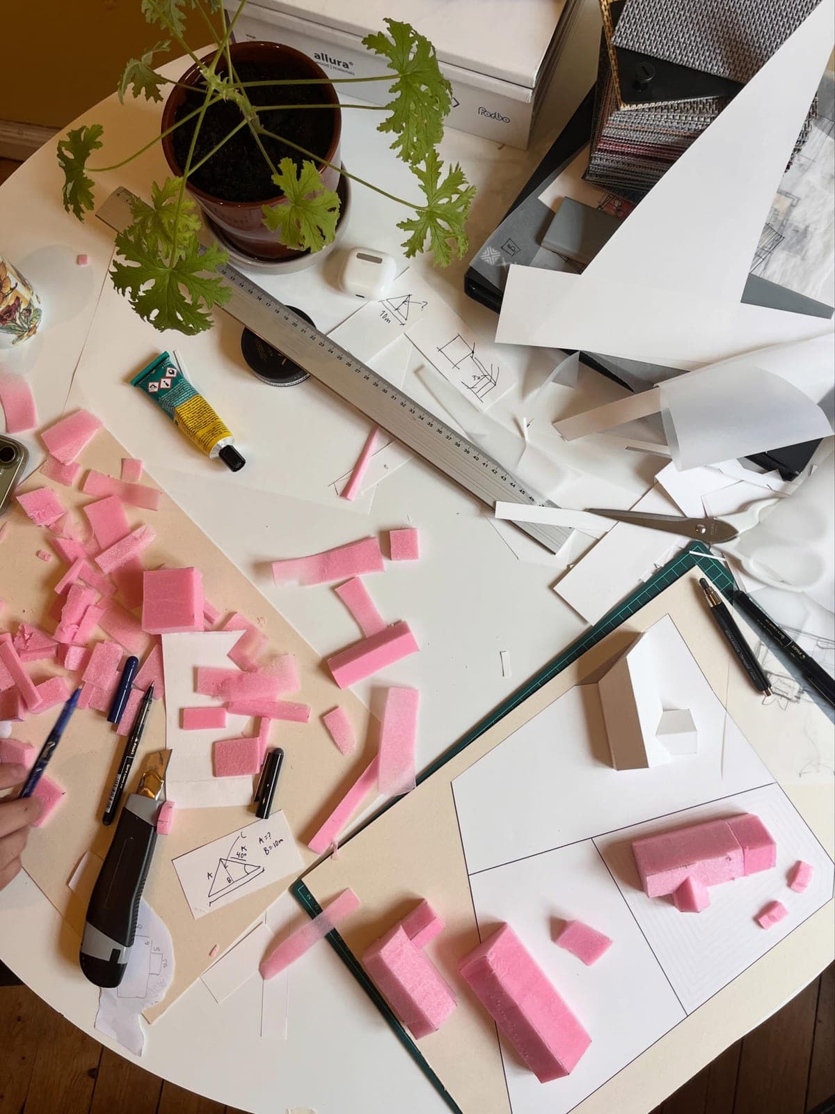 Arbetsbord med rosa skumplastbitar, linjal, skisser och en pappmodell under arbete